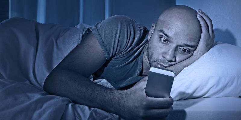 tech neck pain man in bed with phone